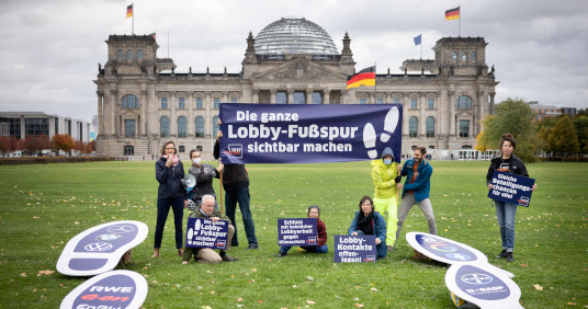 Gruppe von Aktivist*innen mit Banner und übergroßen Fußspuren aus Pappe. Im Hintergrund der Reichstag. Aufschrift Banner: Die ganze Lobby-Fußspur sichtbar machen.