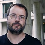 Porträt Johannes Kirsten, Mann mit Bart und Brille im scharzen T-Shirt