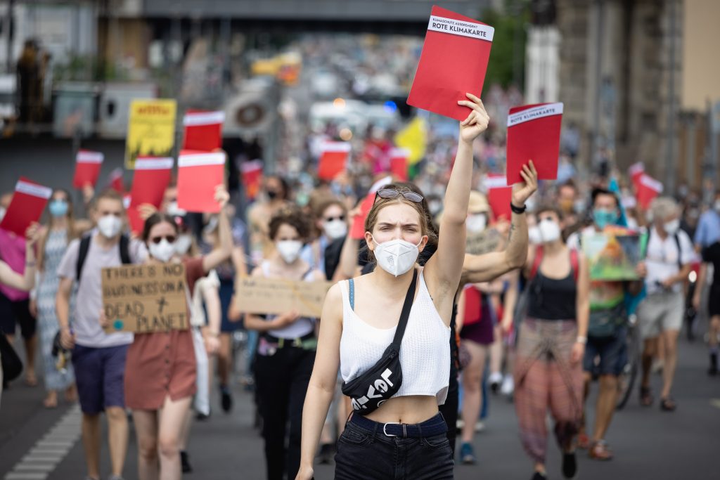 Demonstrant*innen auf der Straße halten rote Schilder in die Höhe. Aufschrift: Rote Klimakarte